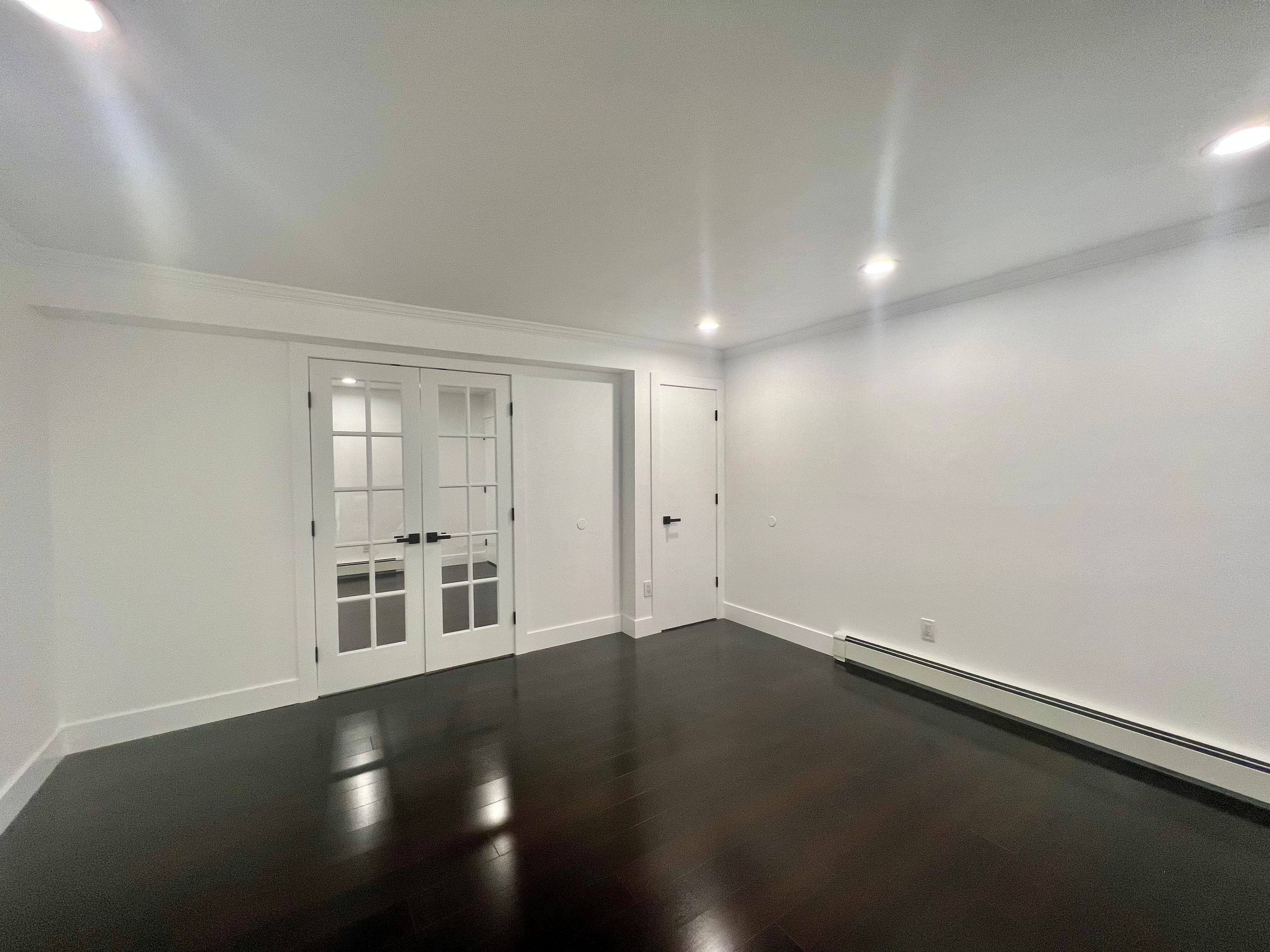 Basement after renovation — white walls, dark floors, French doors with recessed lighting