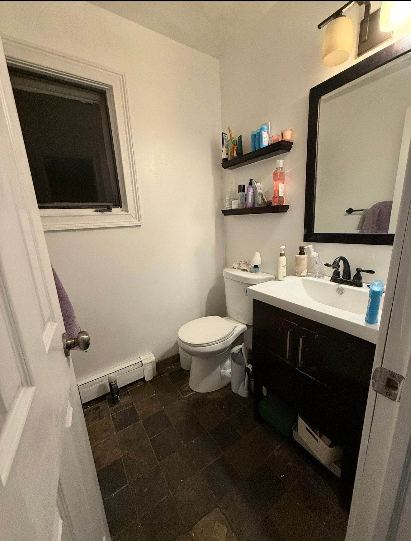 Bathroom before — dark tile floor, cluttered shelves, black vanity